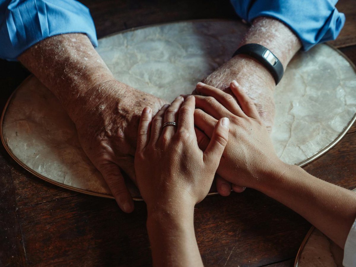 Elderly and younger hands clasped, symbolizing intention carried across generations