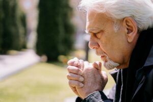 Family member praying quietly beside a hospital bed — proxy pilgrimage for a hospitalized loved one