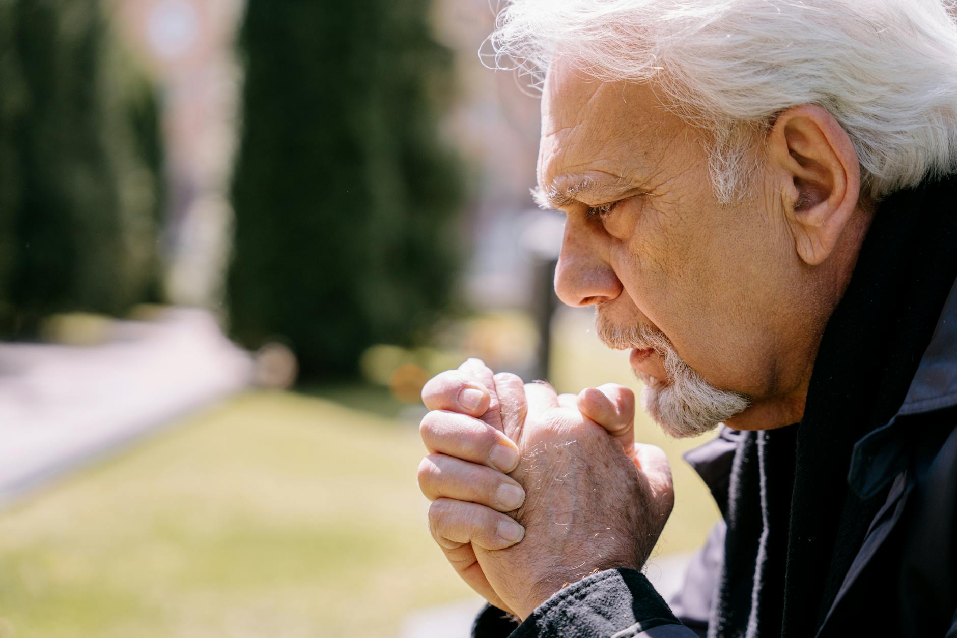 Family member praying quietly beside a hospital bed — proxy pilgrimage for a hospitalized loved one